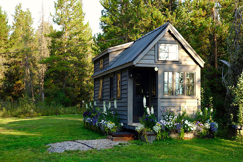 A grey tiny house sits on a grassy yard.