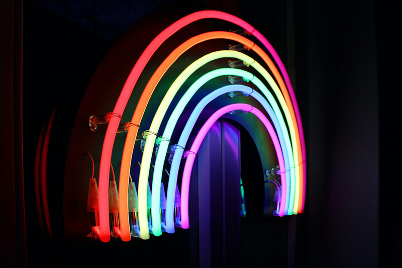 A neon rainbow sign is lit up against a black background.
