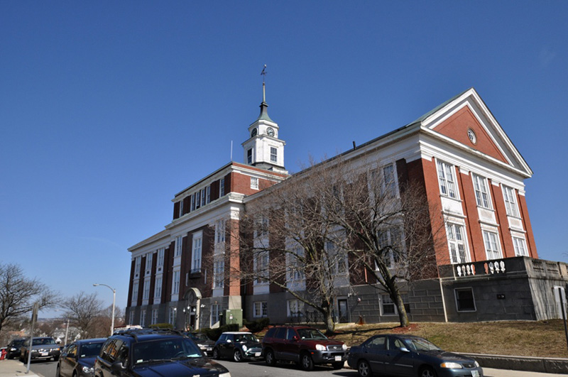 A view of the Somerville City Hall, a multi-story brick building with white trim and a clock tower