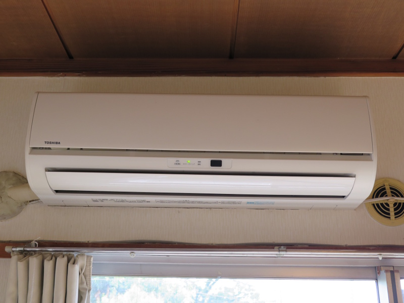 On the short wall above sliding glass doors, a wall mount heat pump in a modest apartment provides heating and cooling without greenhouse gas emissions.