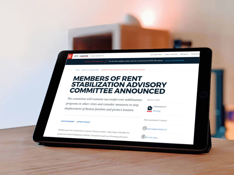 An iPad sits on a table showing a page from the City of Boston website. The page title is “Members of Rent Stabilization Advisory Committee Announced.” The date is March 11, 2022. Derivative of image licensed by Unsplash.