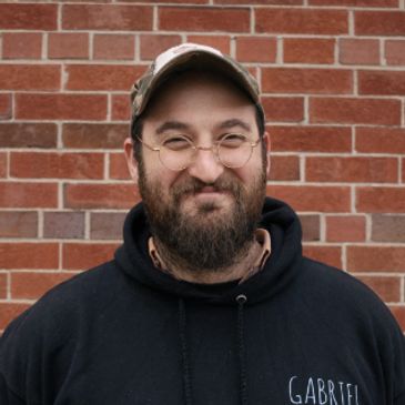 Gabriel Erde-Cohen wears glasses and a full beard. He stands outside in the fall.