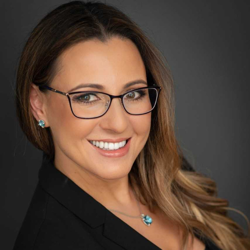 Headshot of Attorney Inessa Shur smiling, wearing glasses, with aquamarine earing and necklace.