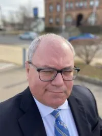 Richard Vetstein wears a suit, glasses and closs-cropped hair. He smiles toughly.