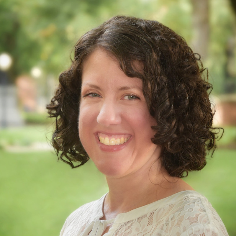 Headshot of Dr. Alicia Wasula outside in summertime smiling and wearing a white blouse.